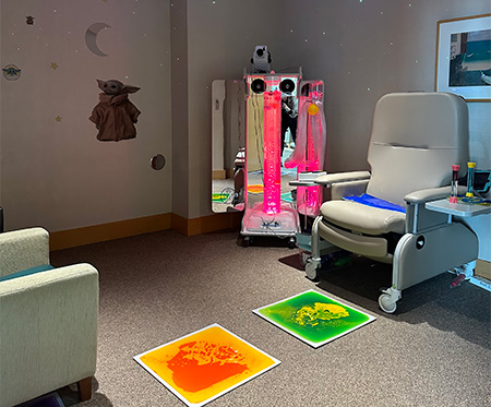 A medical office features a large comfortable chair, sensory mats on the floor and a large sensory station in the corner.