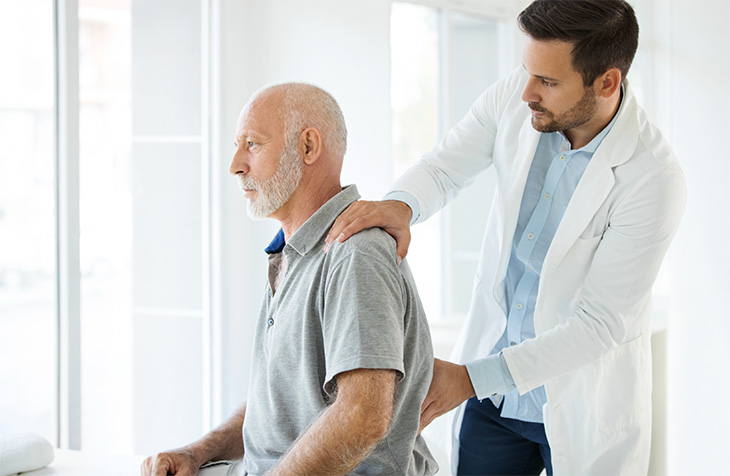 A male clinician examining the back of an older male patient.