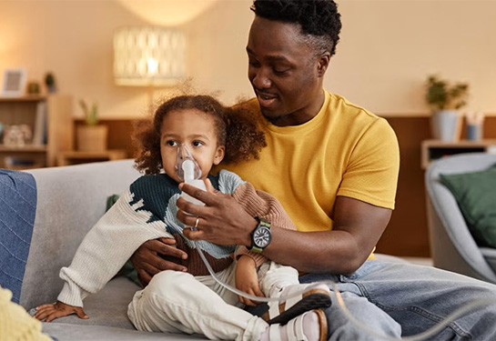 Man holds child with breathing device around nose and mouth.