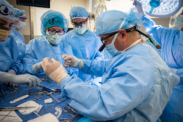 Multiple surgeons in blue gowns and masks operate on a developing baby.