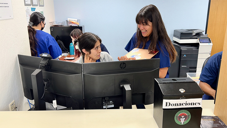 A female student in blue scrubs, right, speaks with another female student in the reception area of the clinic