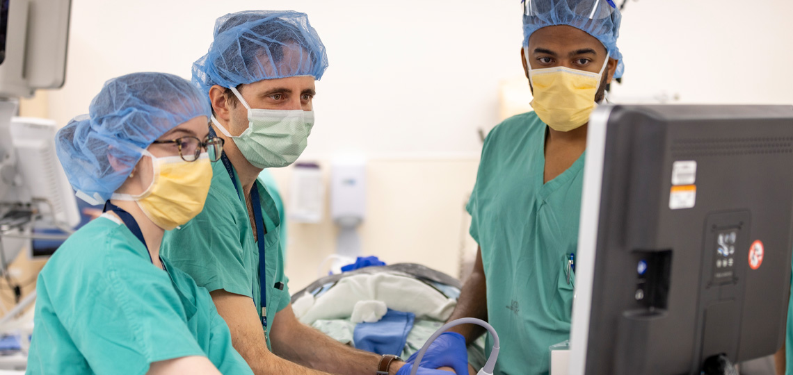 Surgeons wearing green scrubs in operating room look at a computer screen