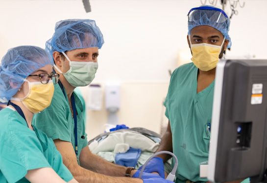 Surgeons wearing green scrubs in operating room look at a computer screen