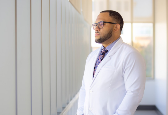 Chris Hall stares with hands in white coat looking out a wall of windows