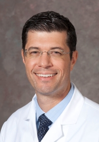 A man in a white coat, light blue shirt and dark blue tie.