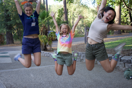 Girl with blonde hair holding hands with two adults while they all jump in the air.