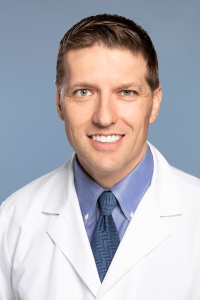 A man in a white coat, blue shirt and blue tie.