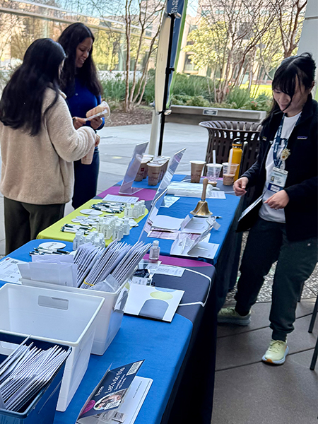 Three students gather around tables covered in blue cloth and paperwork to register for the National Marrow Donor Program