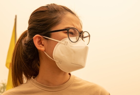 Worried-looking woman wears a mask against a hazy pink background of bad air.