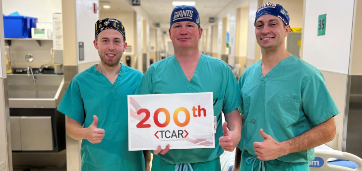 Three people standing together wearing green scrubs holding sign that says 200. 