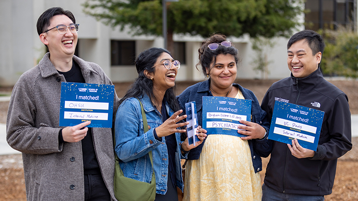 Four students (two men and two women) wearing jackets outdoor hold up their “I Matched” placards