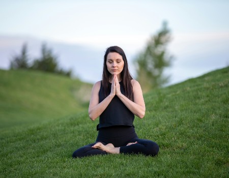 Women with dark hair, sitting in a yoga position on green lush grass