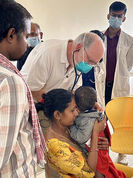 A physician examines a patient while family members stand nearby