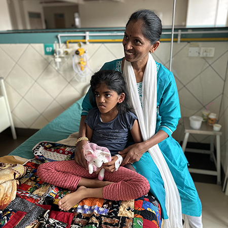 A woman and her daughter sit on a hospital bed in India