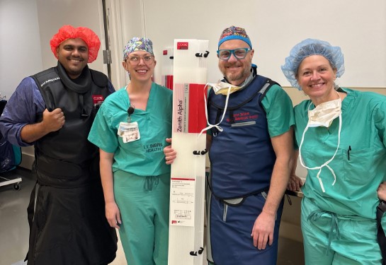 Two people in scrubs and two others wearing lead aprons pose with tall, thin box that says Zenith Alpha.