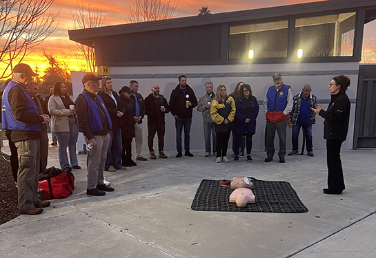 Woman demonstrates how to use AED on a mannequin as a dozen people watch.