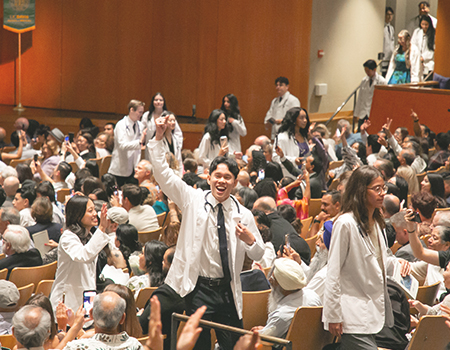 Students march through the Mondavi Center aisles wearing their new, white coats in front of hundreds in attendance