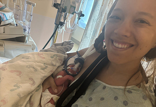 Side view of mother's head as she looks down at her premature baby she is holding in her arms.