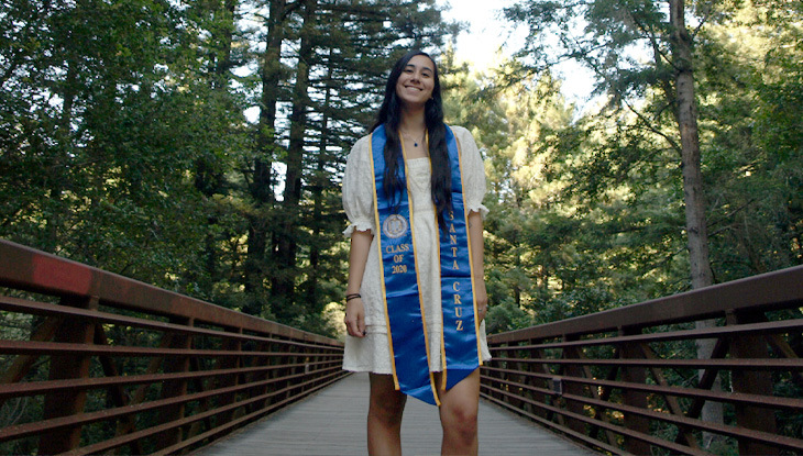 Smiling woman outdoors wearing a light dress and blue academic stole.