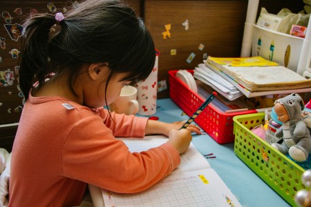 Little girl with black hair drawing on a piece of paper with crayons