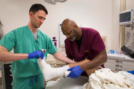 Two medical staff members work together to apply and secure a cast on a patient&rsquo;s lower leg.