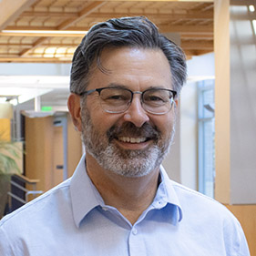 A man in a blue shirt and glasses smiles in the MIND Institute lobby area. 