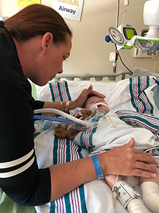 Side shot of mom with a dark blue shirt leaning over hospital crib where baby is hooked up to machines