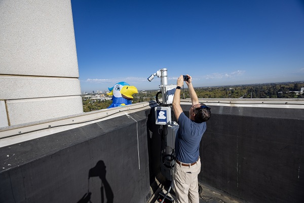 A falcon mascot spreads its wings on a rooftop while a photographer captures images nearby.