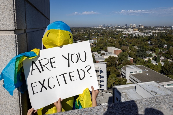 A falcon mascot holds a sign reading &ldquo;ARE YOU EXCITED?&rdquo; above the UC Davis Health campus.