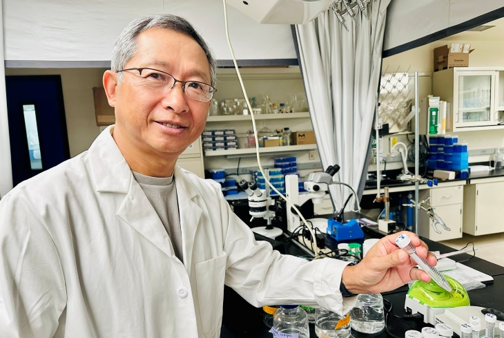 Researcher in a laboratory holding a sample tube beside scientific equipment.