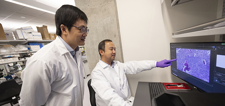 Professor Yuanpei Li is standing behind a researcher who is pointing to a screen with purple imaging.