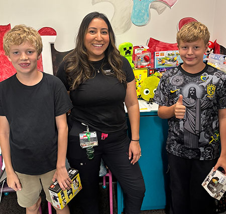 A child life specialist stands between two young boys holding toys after they received a vaccine.