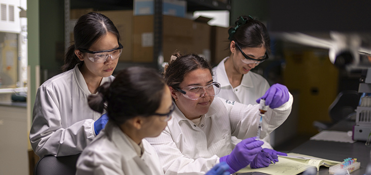 Four researchers wearing white coats, purple gloves and lab goggles are working in professor Yuanpei Li lab at UC Davis Health.