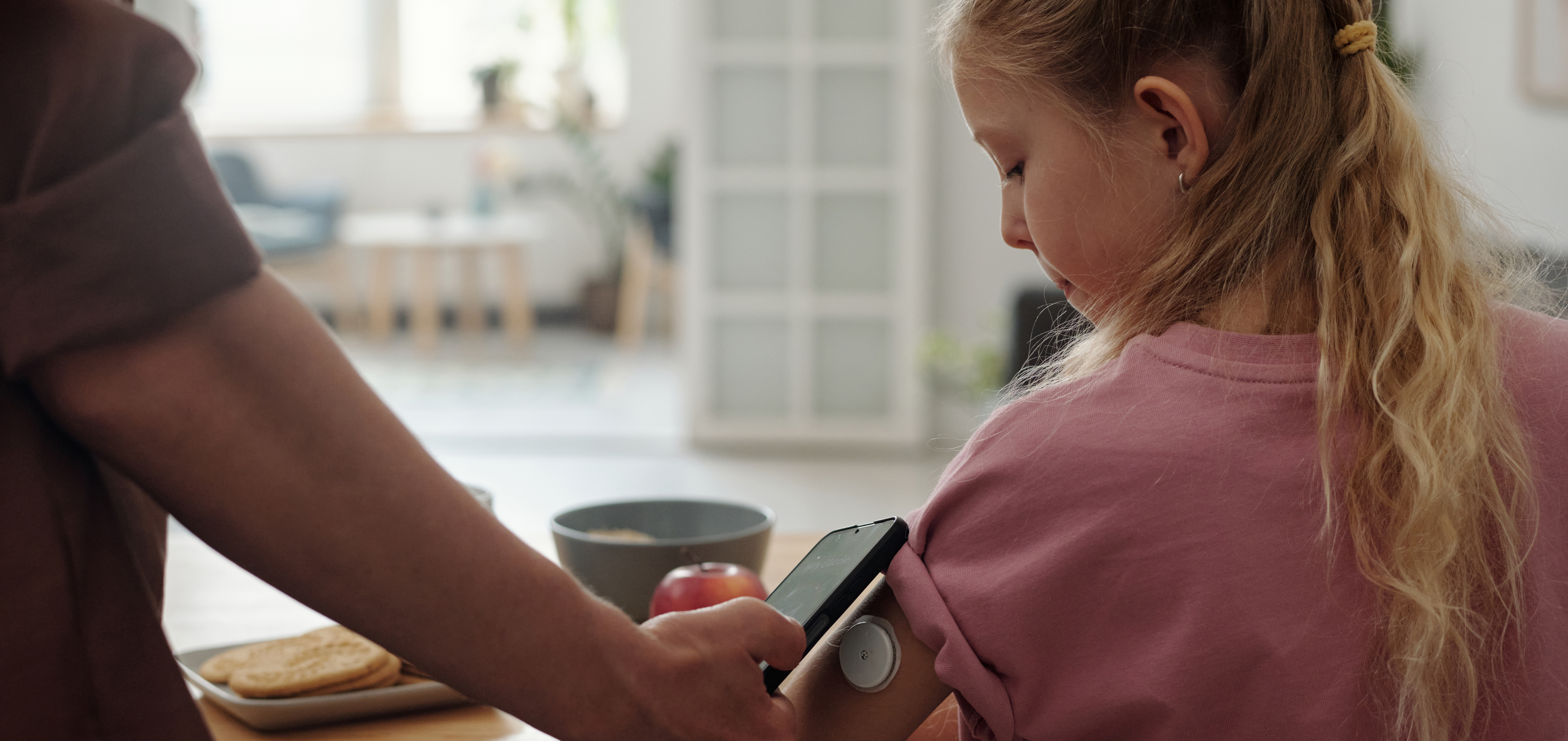 A child wears a continuous glucose monitor. A cellphone is held up to the device. 