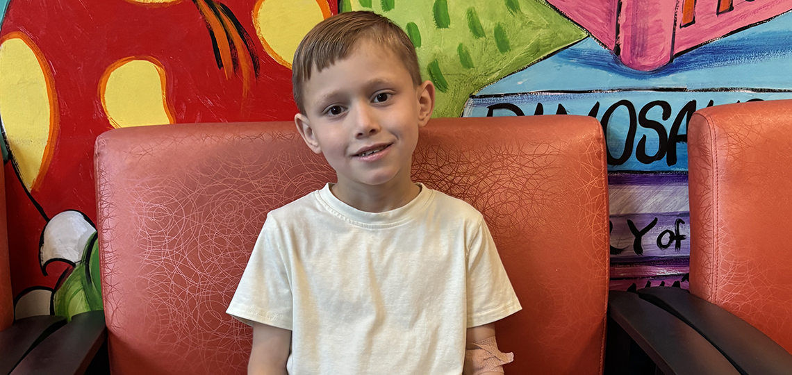Boy with an off white shirt sitting in a chair in front a of colorful background in the doctor's office