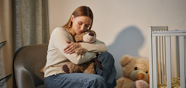 Woman holds teddy bear sitting next to crib