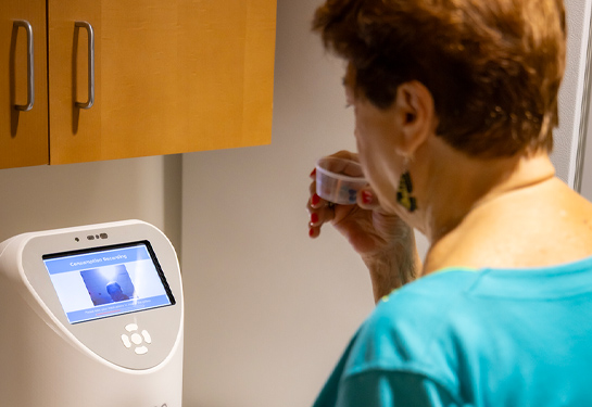 Woman interacts with a smart medication management device while holding a cup with pills to her mouth.
