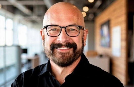 Portrait of Chris Long wearing glasses and a black shirt in an indoor setting.