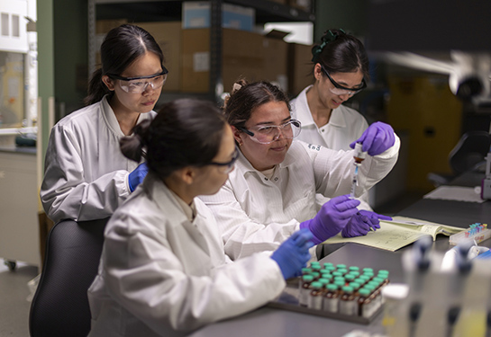Four researchers wearing white coats, purple gloves and lab goggles are working in professor Yuanpei Li lab at UC Davis Health.