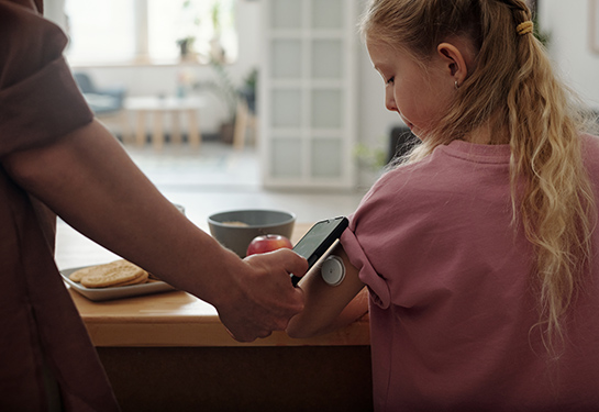 A child wears a continuous glucose monitor. A cellphone is held up to the device. 