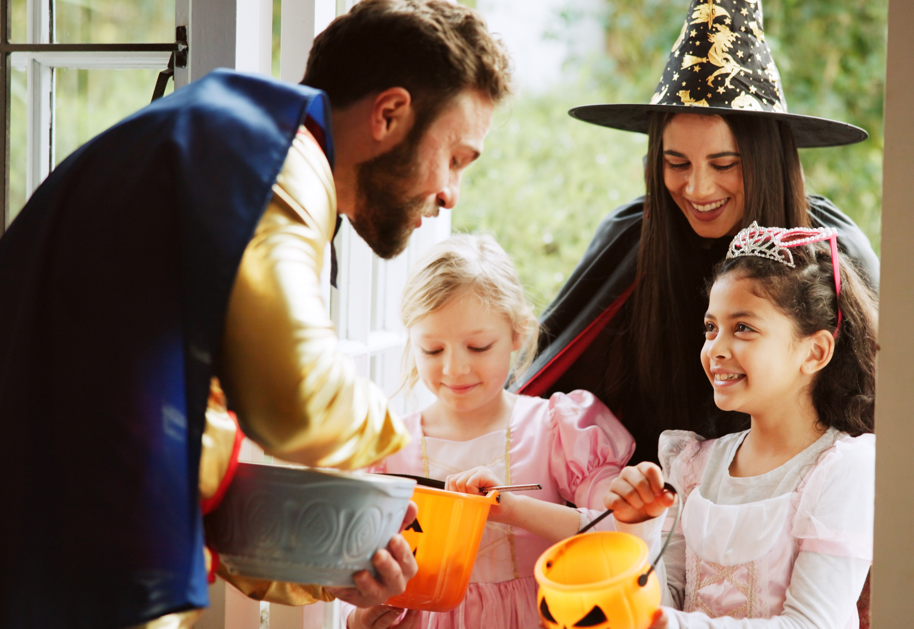 Two children and woman in witch hat stand in doorway while man reaches into bowl.