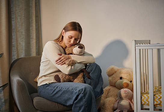 Woman holds teddy bear sitting next to crib