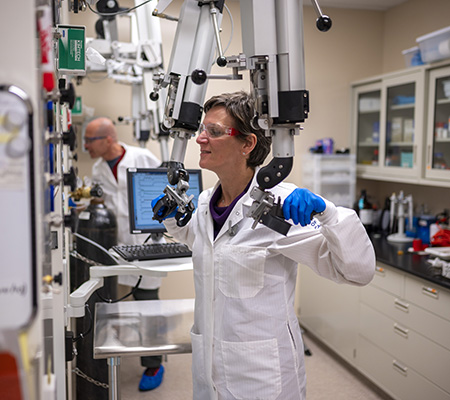 Woman in white coat with goggles grasping handles on an imaging machine.