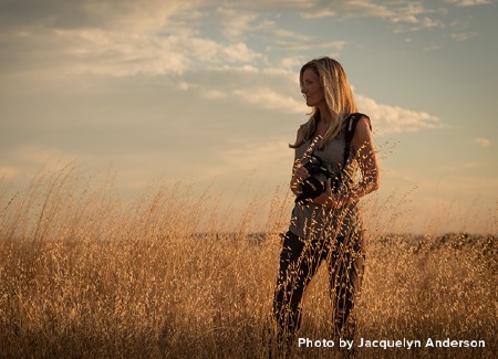 Jacquelyn Anderson outside in the fields holding a camera in her hands