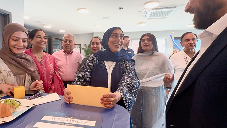 A group of men and women stand around a medical student holding a manila envelope she is about to open