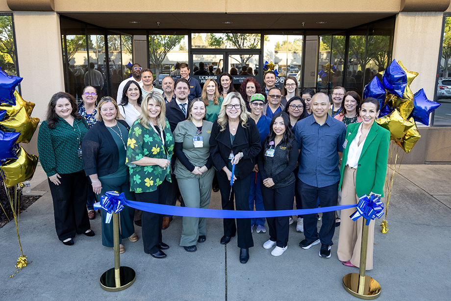 Group of staff and providers gather with scissors to cut blue ribbon