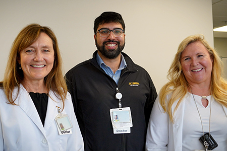 Three individuals standing together, two females on the sides and a male in the middle, smiling at the camera.