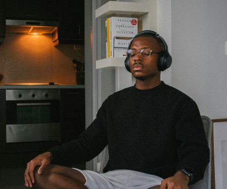 Black man wearing a black long sleeve and shorts, sitting on the floor while wearing headphones