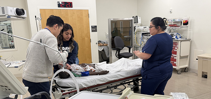 Three medical workers train on a mannequin baby lying on a gurney. 