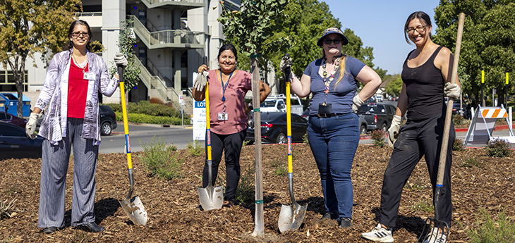 four adults stand outside holding shovels and rakes in a garden on the UC Davis Health campus 